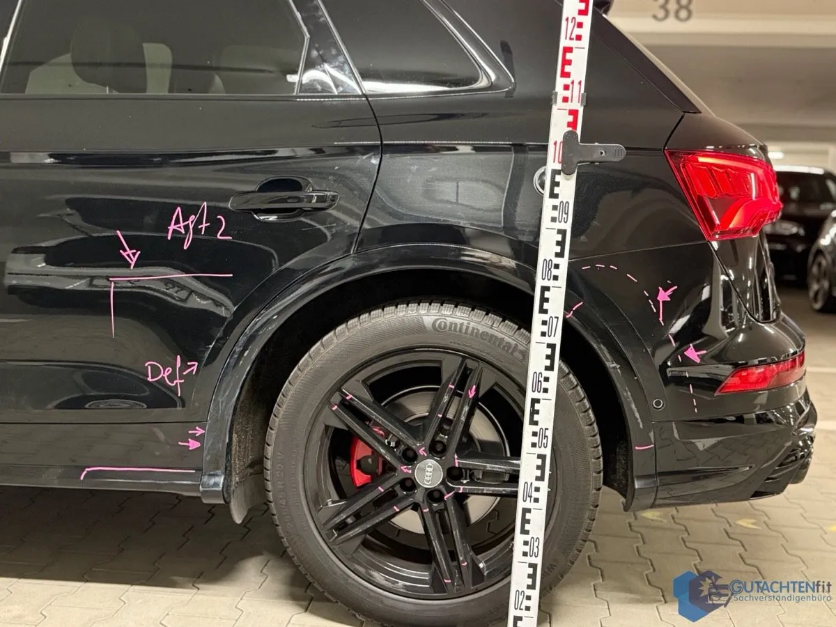 Linke Seite eines schwarzen Audi SQ5 nach einem Unfall, Schäden mit Lackstift markiert, Messlatte an der Seitenwand
