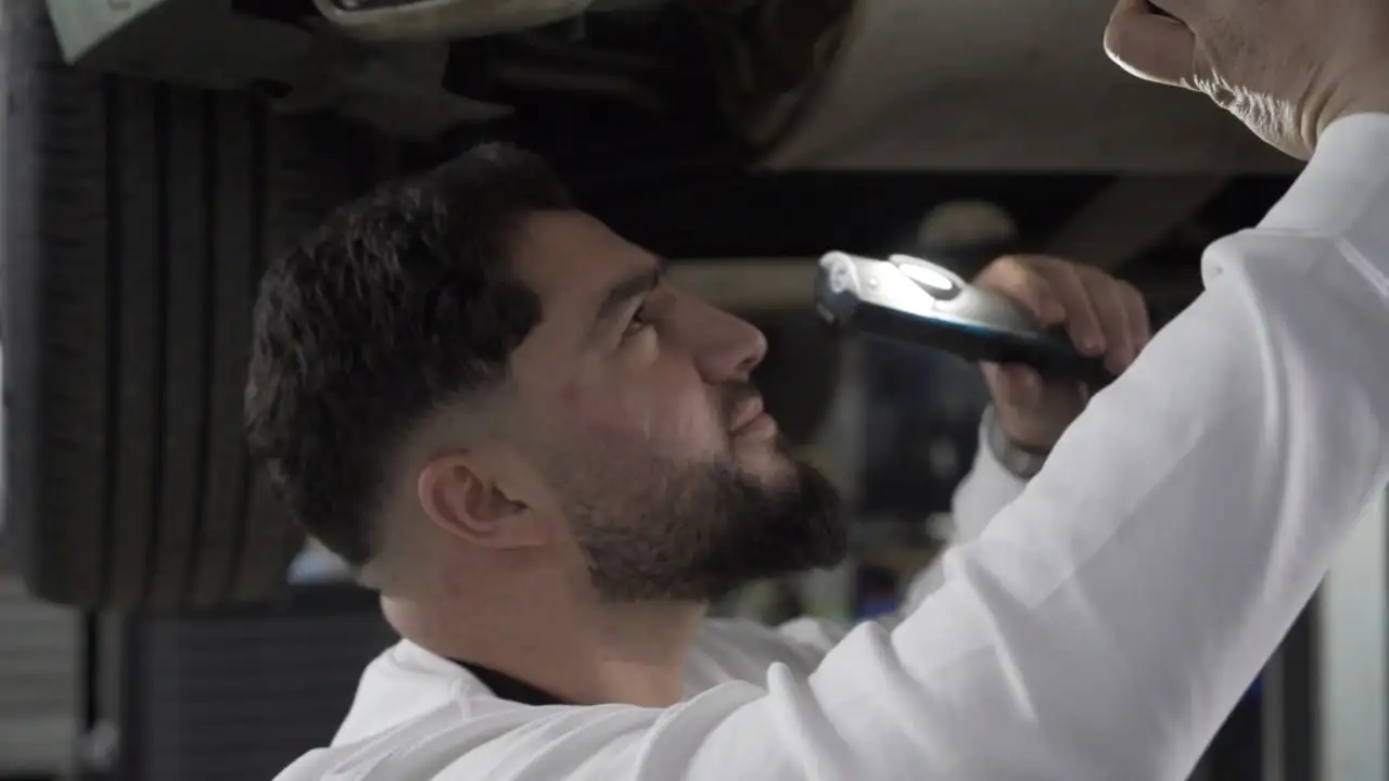 Halis Kaya leuchtet mit einer Prüflampe den Unterboden eines Autos auf der Hebebühne aus