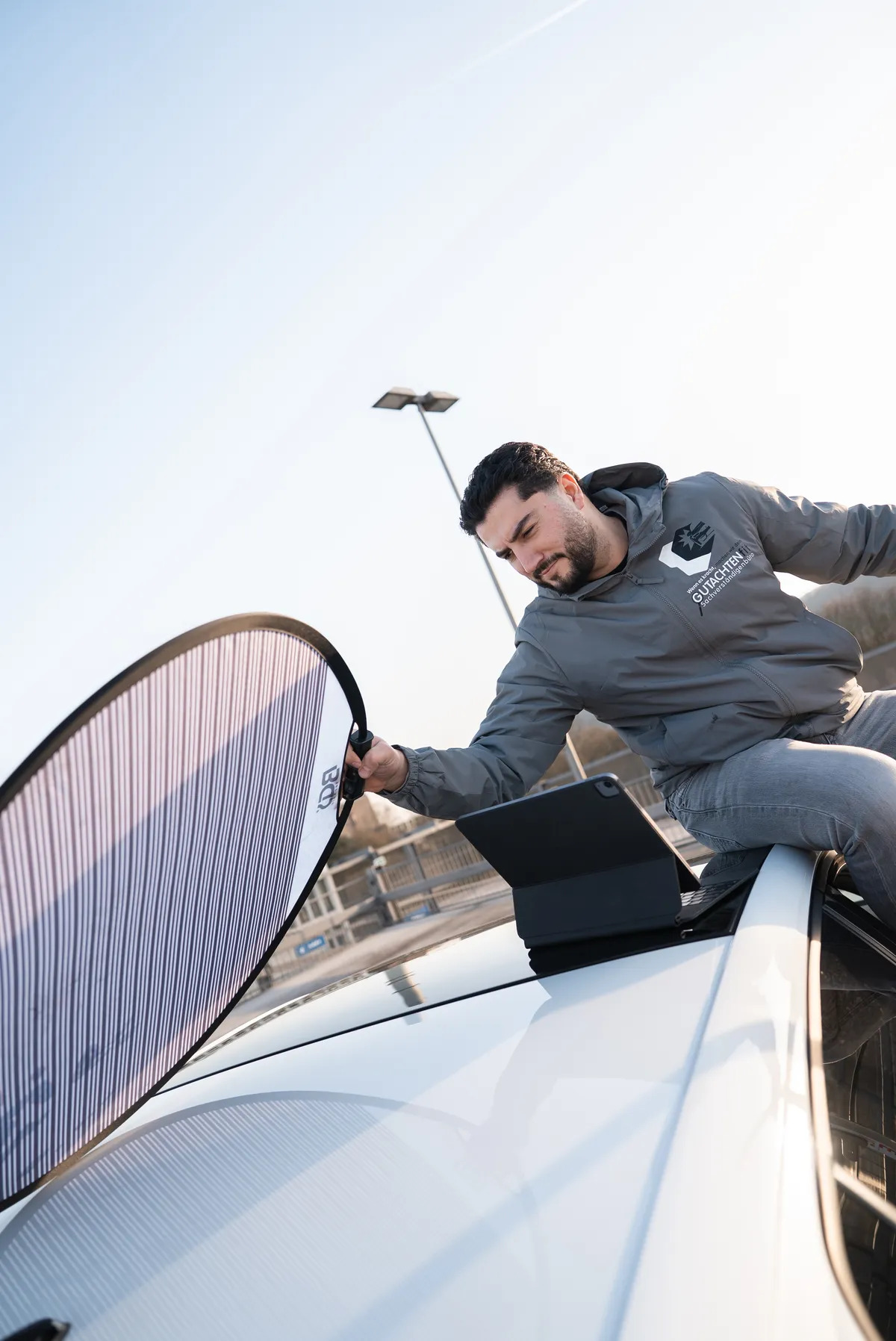 Kfz Sachverständiger dokumentiert Fahrzeugwert mit Tablet und Reflektortafel