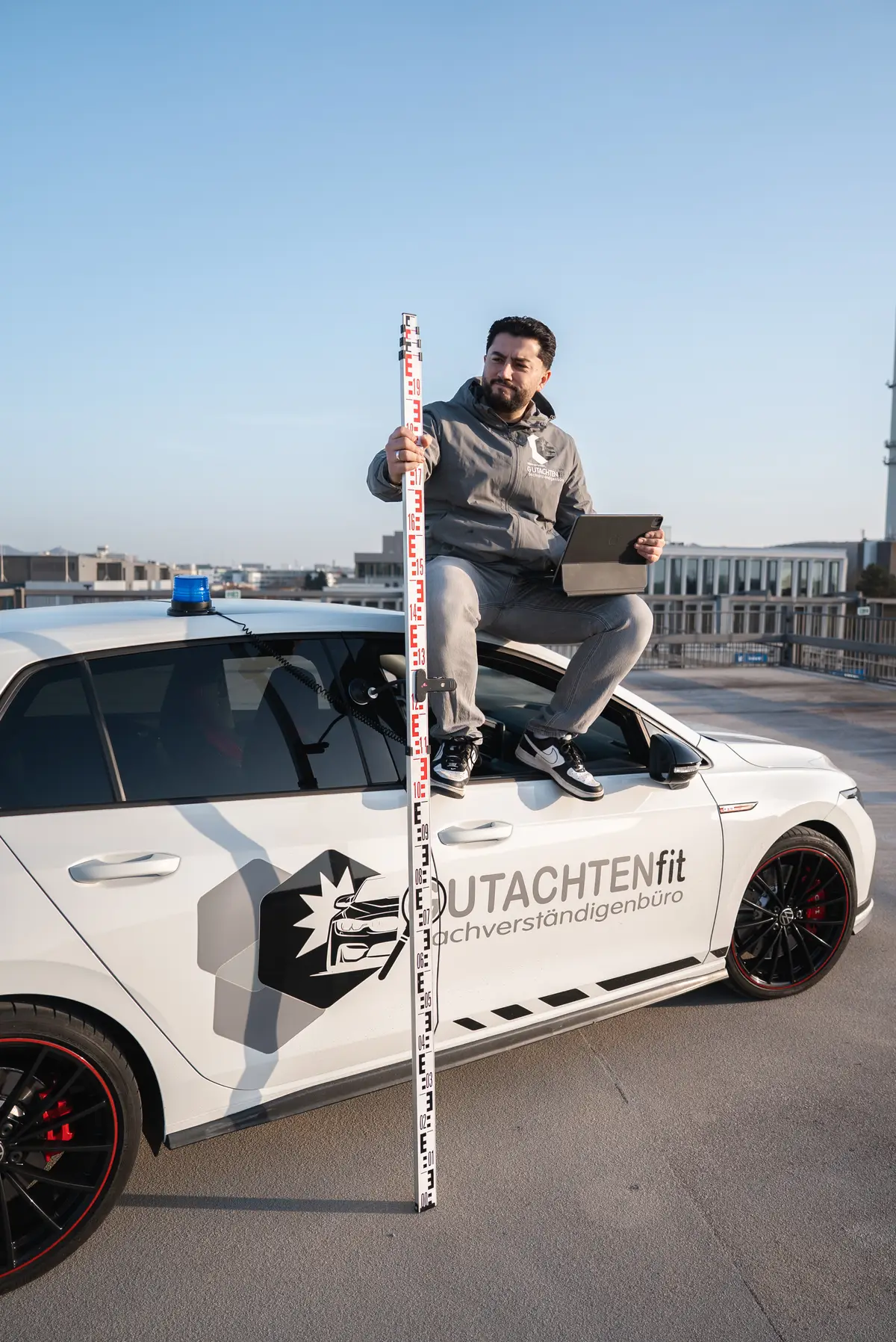 Kfz Gutachter Bonn - Halis Kaya mit Messlatte und Tablet bei der Fahrzeugbegutachtung